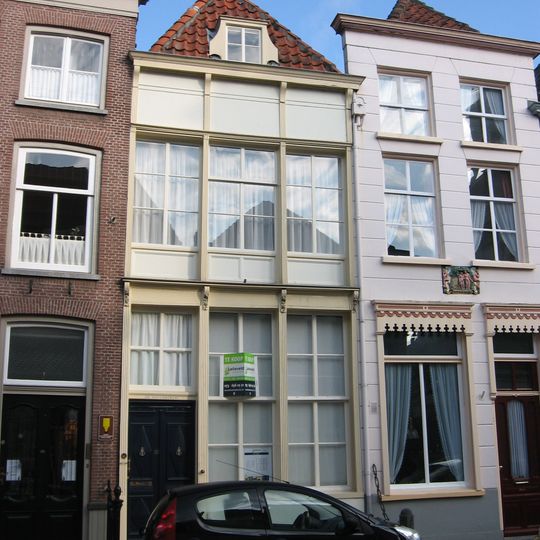 Huis onder schilddak en met lijstgevel die door gegroefde verticale stijlen ingedeeld is waartussen de vensters terugliggen