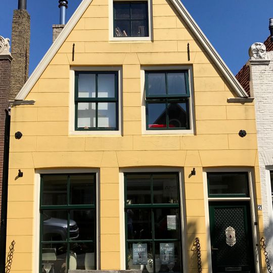 Pand onder zadeldak tegen een tot puntgevel vereenvoudigde en gepleisterde gevel