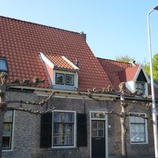 Huis onder zadeldak met langsgevel evenwijdig aan de straat. Schuiframen met negen ruiten