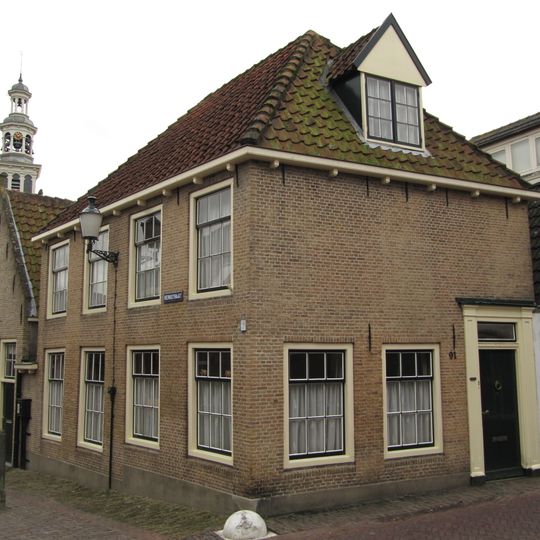 Hoekpand onder schilddak. Oude kozijnen en deuromlijsting door pilasters. Gesneden kalf