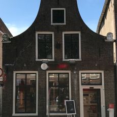 Laag hoekpand onder zadeldak tegen klokgevel met natuurstenen aanzetkrullen en gezwenkte lijst