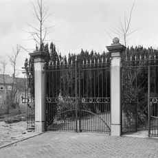 Naast de kerk het toegangshek tot het kerkhof met twee hardstenen hekpijlers,