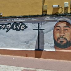 Mural dedicado a un vecino del barrio Portada Alta fallecido en accidente de tráfico. Presenta un retrato del homenajeado junto a una cruz cristiana, el texto «Crazy Life» y el lema «Sólo muere quien cae en el olvido!».