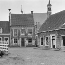 Pand, bestaande uit begane-grond met hoog zadeldak tussen puntgevels met vlechtingen. In de gepleisterde voorgevel een sieranker en een deuromlijsting met pilasters en hoofdgestel. Gevelsteen
