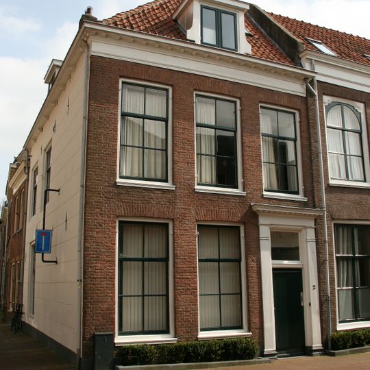 Hoekpand met verdieping, schilddak en eenvoudige lijstgevel. Deuromlijsting met pilasters en bovenlicht