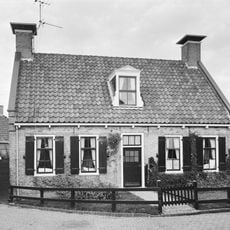 Laag pand onder zadeldak tussen topgevels met schoorstenen waarop borden en met dakkapel met klauwstukken en driehoekig fronton