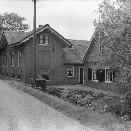 Boerderij, dwarshuis met gebogen houten daklijsten, chaletachtig model. Bijgebouw met houten topgevel