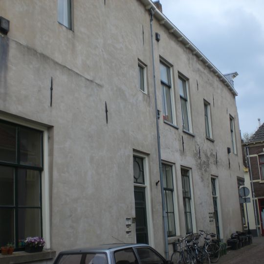 Omvangrijk, uit twee bouwlichamen samengesteld, in aanleg laat-gotisch hoekhuis