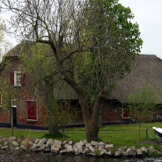 Rustiek gelegen boerderij onder rieten wolfdak. Op het erf een oude roedenberg