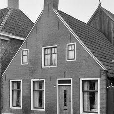 Pand tegen brede topgevel onder zadeldak met topschoorsteen