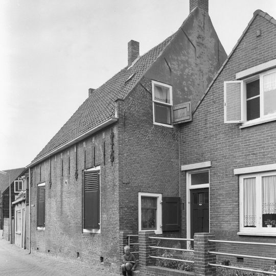 Pand onder zadeldak waarvan een van de zijtoppen vlechtingen vertoont en de andere is vernieuwd