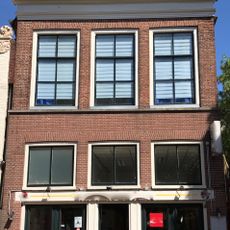 Pand onder zadeldak met topschoorsteen en gevel met rechte kroonlijst boven moderne pui