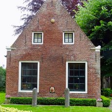 Pandje met twaalfruitsvensters onder zadeldak tegen topgevels met vlechtingen in kopjes