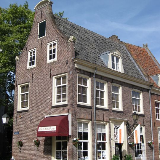 Hoog huis, gepleisterd in klokgevel, uitlopend zadeldak
