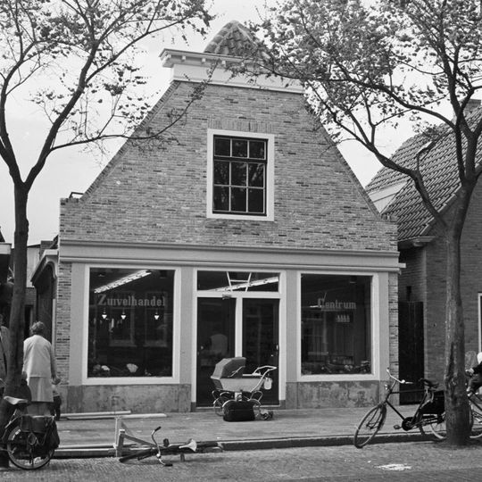 Breed pand met verdieping onder zadeldak tegen afgeknotte gepleisterde puntgevel