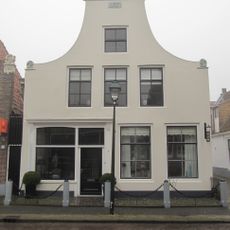 Pand met gepleisterde klokgevel met aanzetkrullen en driehoekig fronton