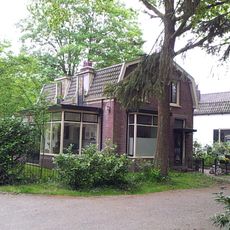 Verdiepingloos pand onder mansarde dak; daterend uit de bouwtijd van de kerk. Maakt deel uit van een groepsbebouwing aan het Kerkplein