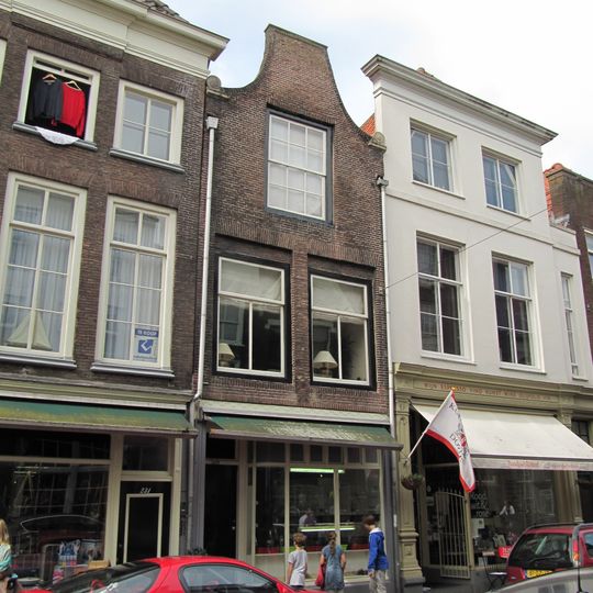 Pand met eenvoudige tuitgevel met rollaag, eindigend in natuurstenen voluten op geprofileerde dekplaten en bekroond door een rechte lijst