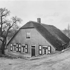 Boerderij, onder rieten wolfdak. In de gepleisterde voorgevel vensters met luiken en 20- en 16-ruitsschuiframen