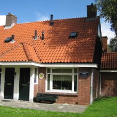 Blok met 9 woningen, gecombineerde toegangen van twee woningen onder een ingestoken schilddak, zijkant met houten topgevel, onderdeel van complex bejaardenwoningen in Tuindorp Nieuwendam