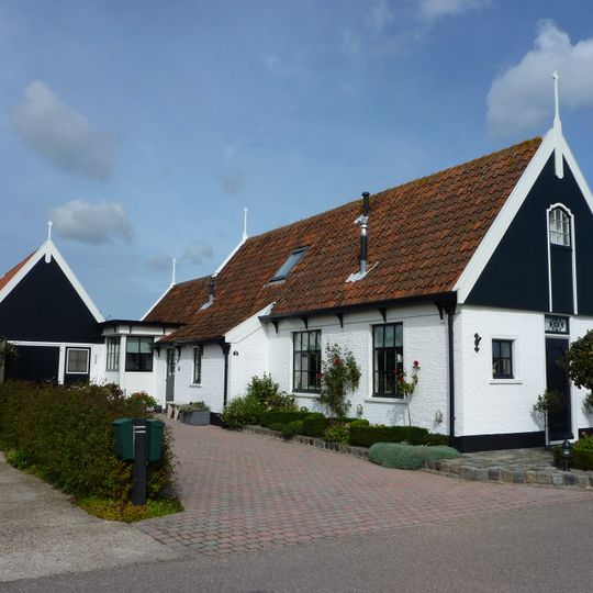 Vissershuis onder zadeldak met houten voorschot en zolderluik. Twee negenruits vensters