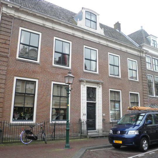 Vijf traveeën breed eenvoudig pand met hoeklisenen; rechte kroonlijst en dakkapel. Omlijste deurpartij met snijraam. Stoephek langs de volle breedte, pompvoet op de stoep