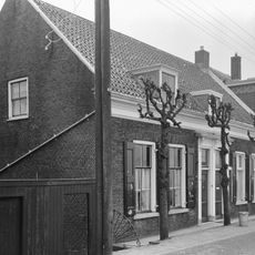 Dwarshuis van begane-grond met hoog schilddak. Deuromlijsting met hoofdgestel op gesneden consoles. Vensters met luiken en zesruitsschuiframen. Vormt een geheel met het buurnummer 277