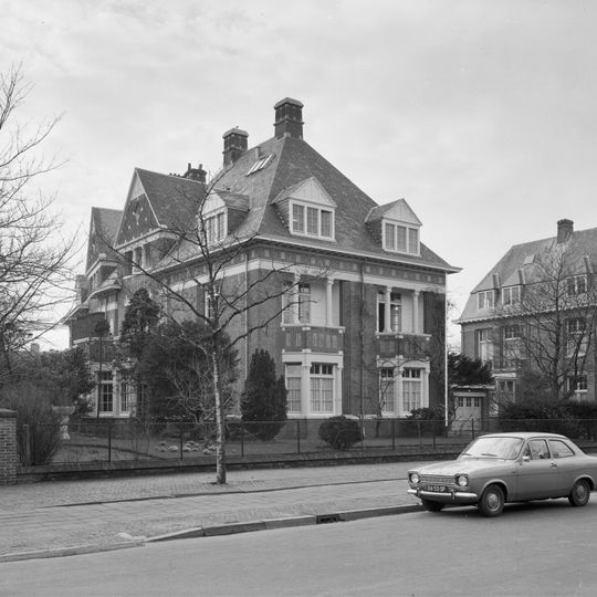 Helft van een vrijstaand bouwblok bestaande uit twee symmetrische in de diepte van een smal kavel geschakelde villa's in een historiserende bouwstijl