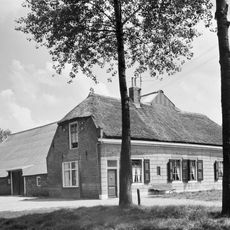 Boerderij. Dwars woonhuis onder rieten wolfdak en met gepleisterde voorgevel onder houten lijst. In de zijgevels sierankers en in de rechterzijgevel een half kruiskozijn.